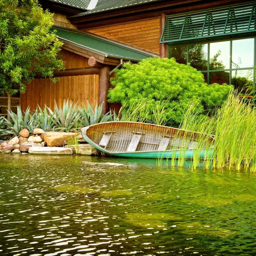 Jardin aquatique avec barque flottante devant un bâtiment en verre et bois